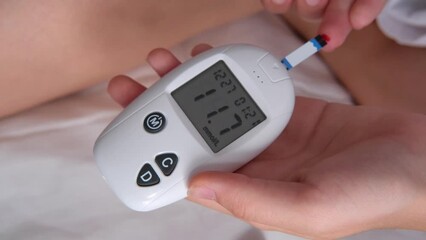 Teenage girl measures blood glucose level on bed at home.