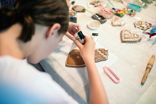 Girl decorating gingerbread cookies with icing sugar. Selective focus.