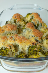 Baked broccoli with cheese and eggs in a glass bowl on a white table. Healthy vegetable food rich in vitamins and microelements. Home kitchen.