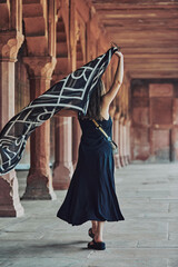 East asian woman in black dress dancing with translucent scarf among columns of ancient indian temple, touristic walking in Taj Mahal of attractive happy young girl, joyful tourism in India