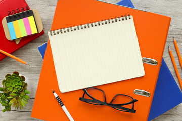 Blank notepad and pen on an orange folder with glasses on a wooden table. Top view with copy space in bright light colors, flat lay.