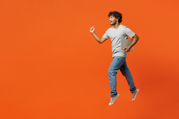 Fototapeta na wymiar Full body side view young fun happy Indian man wearing t-shirt casual clothes jump high hold closed laptop pc computer run isolated on orange red color background studio portrait. Lifestyle concept.