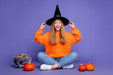 Full length photo of youth girl touching black witch hat posing for halloween season trick or treat...