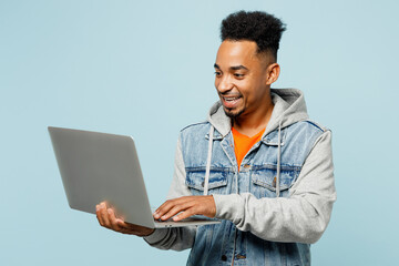 Young IT man of African American ethnicity wear denim jacket orange t-shirt hold use work on laptop...