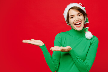 Young woman wears cozy green turtleneck Santa hat posing point hands arms aside indicate on...