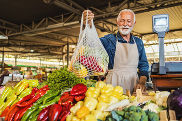 Portrait of a senior man holding a reusable bag full of fresh produce in a farmer's market.