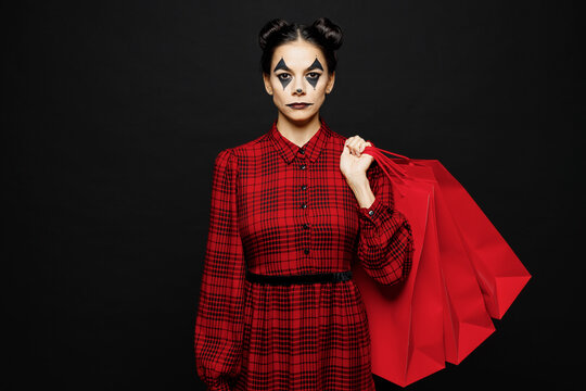 Young woman with Halloween makeup face art mask in clown costume red dress hold paper shopping package bags isolated on plain black background studio Scary holiday party concept sale buy day concept
