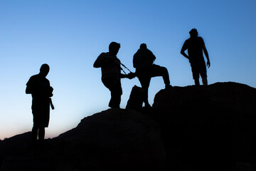 silhouette of Group of male photographers standing or taking photograph on top the mountain in evening sunset with blue sky on the background - obrazy, fototapety, plakaty