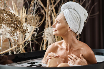 relaxed middle aged woman with white towel on head taking bath in modern apartment, spa day