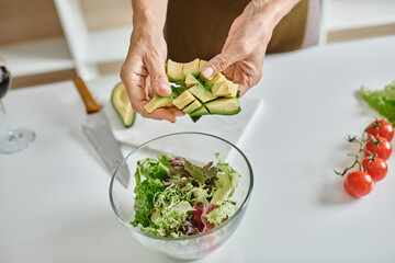 cropped woman holding sliced ripe avocado near lettuce in bowl and glass of red wine, close up