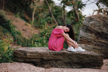 Beautiful woman in pink dress sitting on a big stone near the sea