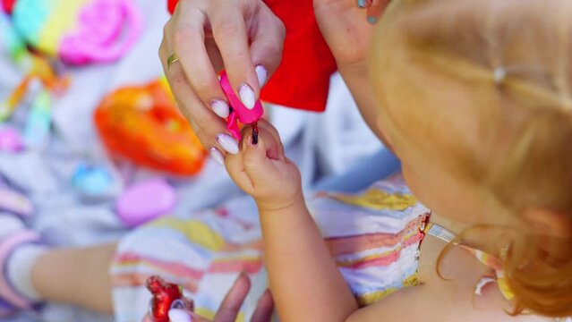 A close-up of a mother painting her daughter's nails with nail polish. They spend time together in the fresh air. High quality 4k footage