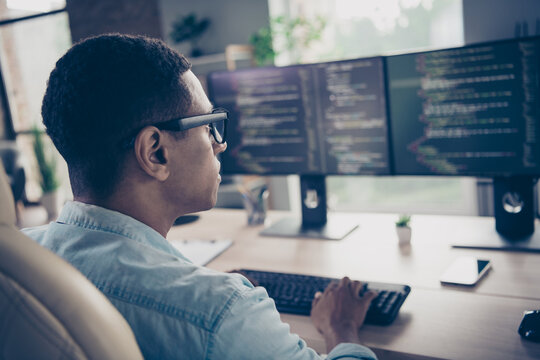 Rear photo of smart skilled young man worker qa engineer testing open data code typing keyboard looking computer monitors in office room