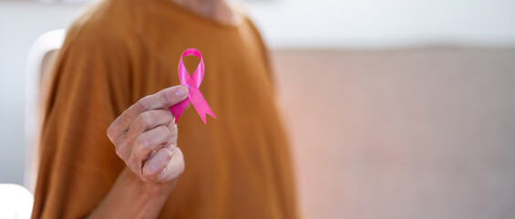 Naklejka premium Portrait of confident smiling elderly senior woman with pink ribbon at her home. Health care, support, prevention. Breast cancer awareness month concept
