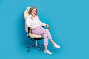 Full length photo of positive thoughtful woman dressed white shirt eyewear sitting chair empty space isolated blue color background