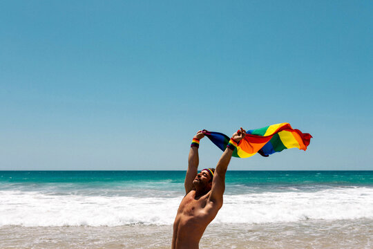 Serious man with rainbow flag in beach