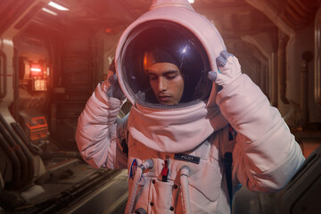 Male astronaut in spacesuit touching helmet with closed eyes while standing in spaceship