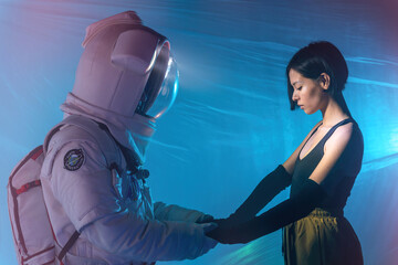 Anonymous astronaut in spacesuit and woman in casual clothes standing and holding hands