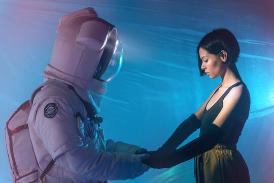 Anonymous astronaut in spacesuit and woman in casual clothes standing and holding hands