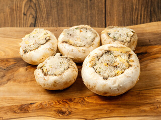 Stuffed mushrooms cups on a wooden board and table. High quality product with breadcrumbs, cheese and herbs ready for oven cooking.