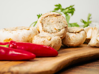 Stuffed mushrooms cups and chilly peppers and garlic cloves on a wooden board and table. High...
