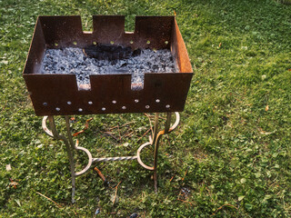 Hand custom made metal grill for barbeque standing on a green grass in a park. Meal preparation device to use firewood.