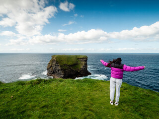 Girl looking at stunning nature scene with cliffs, Atlantic ocean and low cloudy sky on sunny day....