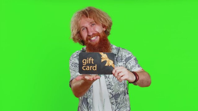 Happy caucasian man showing pointing on gift discount certificate voucher coupon for store holidays sale. Redhead guy with shopping christmas surprise card isolated on green chroma key background