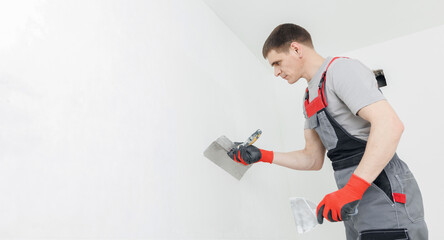 Builder with plastering tools indoors for renovation apartment, white walls with worker banner