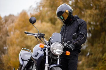 Papier Peint photo Moto motorcyclist in motorcycle gear and helmet near a classic motorcycle in autumn
