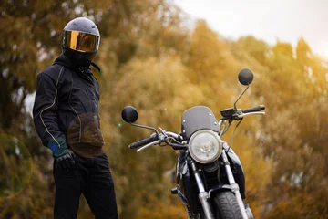 Cercles muraux Moto motorcyclist in motorcycle gear and helmet near a classic motorcycle in autumn