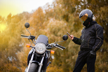 motorcyclist in motorcycle gear and helmet near a classic motorcycle in autumn