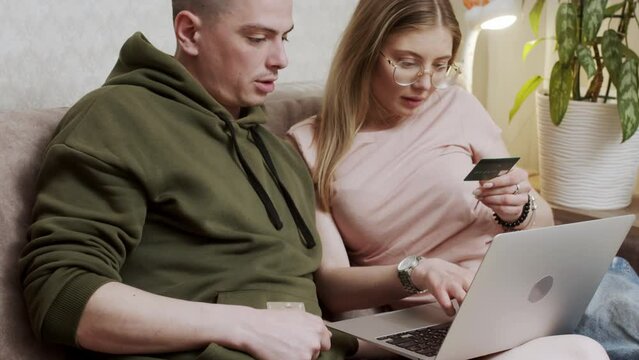 Happy online retail web services buyers make easy purchase, instant money transfer, use secure remote e payment concept. Couple in love sit on sofa with laptop holding credit card buying on internet