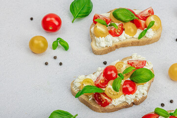 Fototapeta na wymiar Fresh bread sandwiches with tomato cherry, cream cheese and basil leaves. Morning breakfast concept
