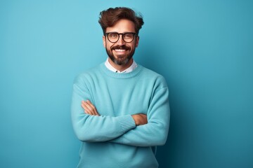 Young handsome man with beard wearing casual sweater and glasses over blue background happy face smiling with crossed arms - obrazy, fototapety, plakaty