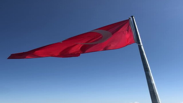 The Turkish flag waving proudly in the blue sky. The waving of the flag displays a beautiful scene reflecting the feelings of national pride and independence.