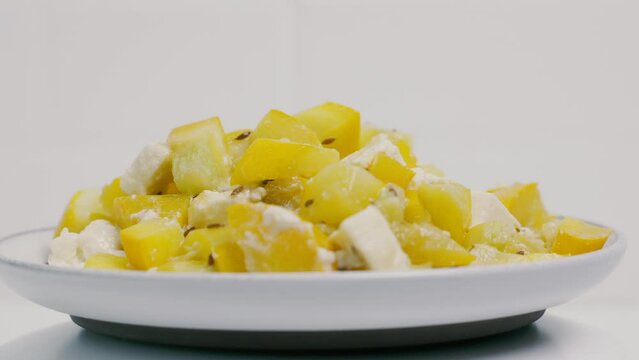A white plate with a prepared dish of zucchini and feta cheese is spinning on the turntable. Close-up, presentation.
