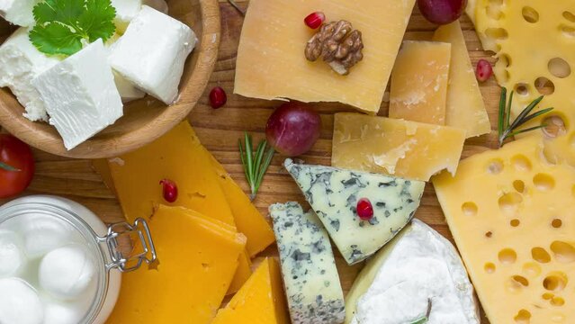 Assortment cheeses on wooden cutting board. Cheese plate served with grape fruits, tomatoes and rosemary, various cheese on a platter. top view