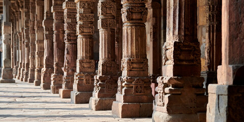 Stone columns with decorative bas relief of Qutb complex in South Delhi, India, close up pillars in ancient ruins of mosque landmark, popular touristic spot in New Delhi, ancient indian architecture