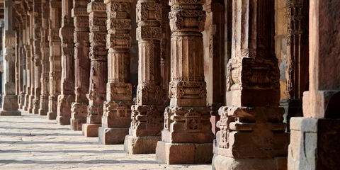 Fotobehang Stone columns with decorative bas relief of Qutb complex in South Delhi, India, close up pillars in ancient ruins of mosque landmark, popular touristic spot in New Delhi, ancient indian architecture © TRAVELARIUM