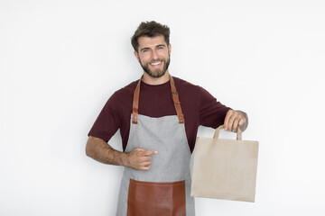 Man barista waiter in apron and t-shirt working in coffee shop point at blank craft paper takeaway bag, mockup. Business startup concept