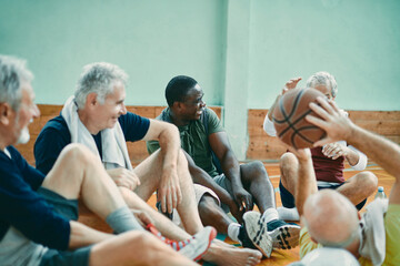 Diverse group of male senior friends sitting on the floor of a gym after playing basketball