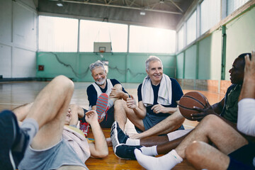 Diverse group of male senior friends sitting on the floor of a gym after playing basketball