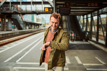 Middle aged man looking at his watch and expecting the arrival of his train at the train station