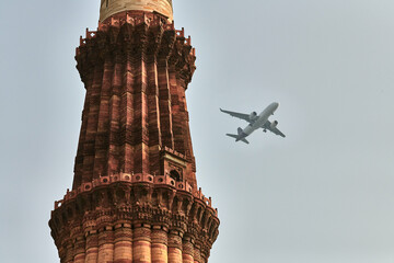 Qutb Minar minaret with airplane in sky background, tower part Qutb complex in South Delhi, India, big red sandstone minaret tower landmark popular touristic spot in New Delhi, tallest brick minaret - obrazy, fototapety, plakaty