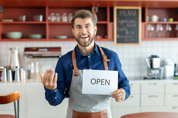 Successful small business owner man standing in coffee shop, keep the sign open and inviting to his...