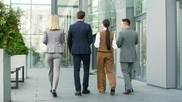 Rear back view of a business team people walking near office center chatting. Diverse Group of employees in formal suit during a break in a meeting or conference communicate speak and talk while going