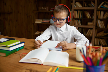 Cute little schoolboy student in headset doing language homework at home