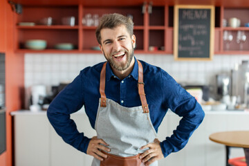 Portrait of excited handsome european male barista standing at coffee cafe counter and smiling at camera, coffee shop owner - obrazy, fototapety, plakaty