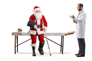 Santa claus with injured leg and arm sitting on a mat table and doctor writing a document